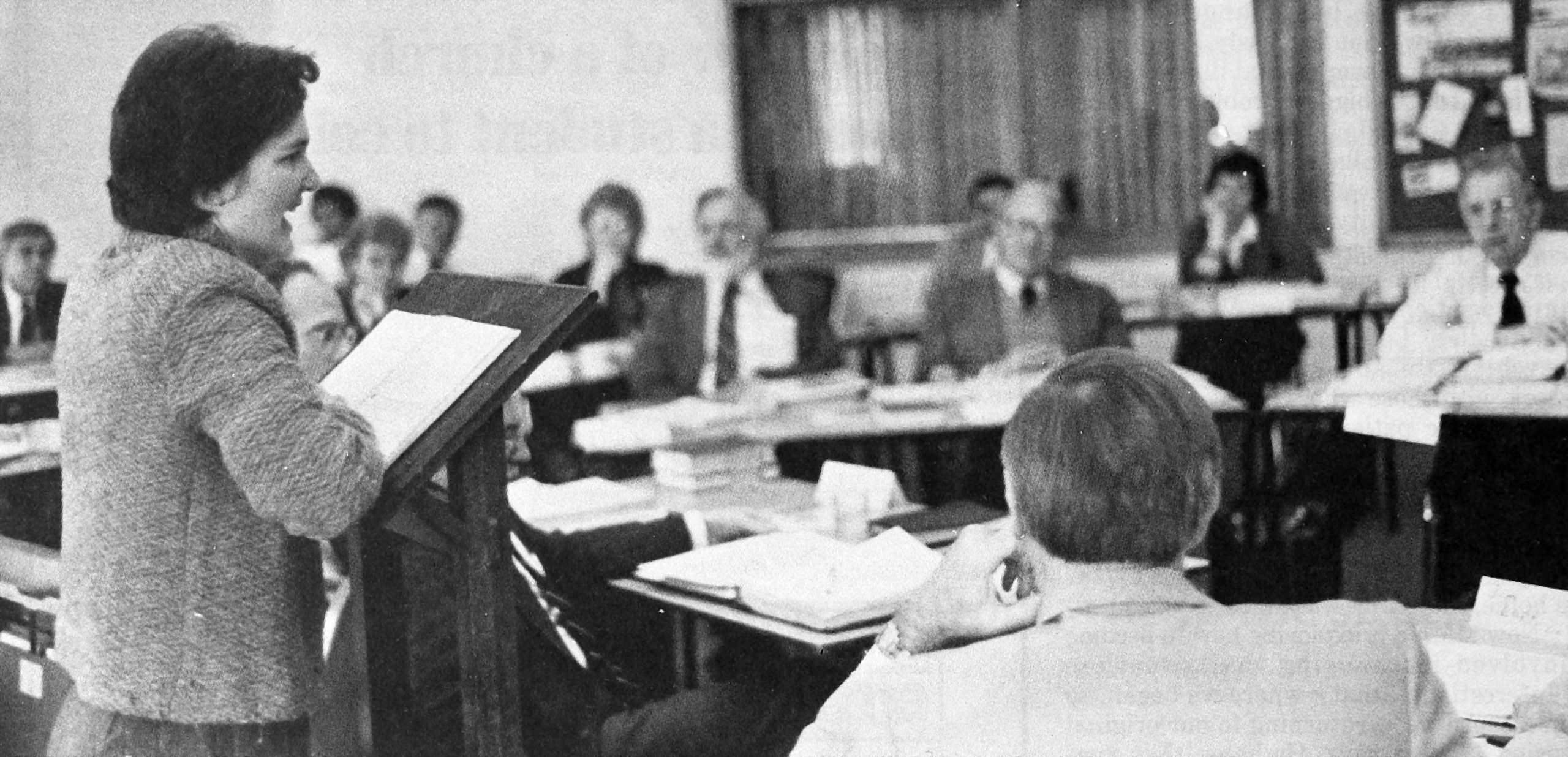 Chris Longenecker, standing at a podium, addresses a group seated at desks