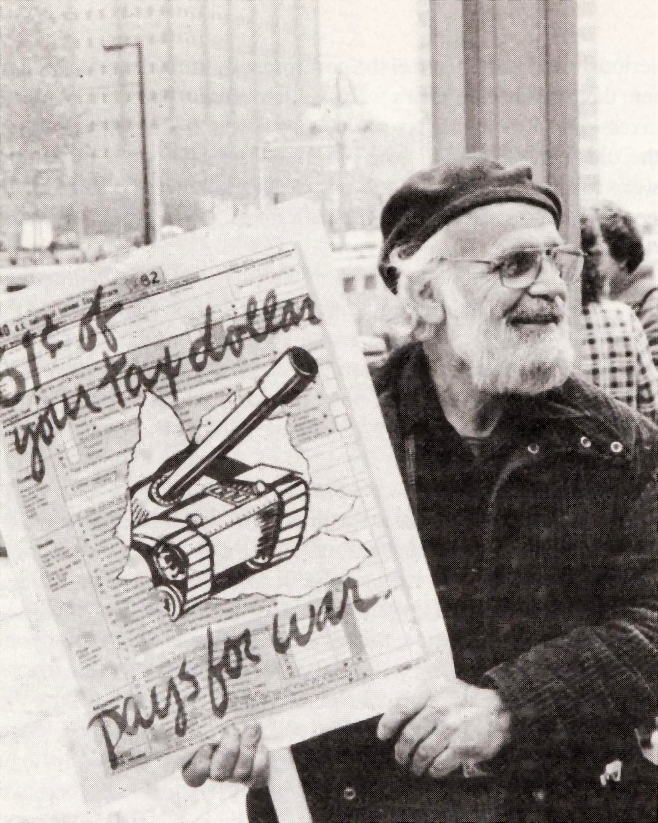 George Willoughby holding a picket sign that reads “61¢ of your tax dollar pays for war” with an illustration of a tank bursting through a 1982 income tax form