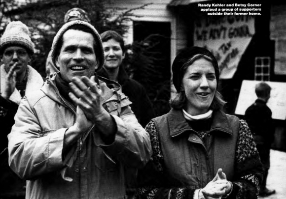 Randy Kehler and Betsy Corner applauding with others standing behind them, outdoors in front of their home which has a banner hanging from it.