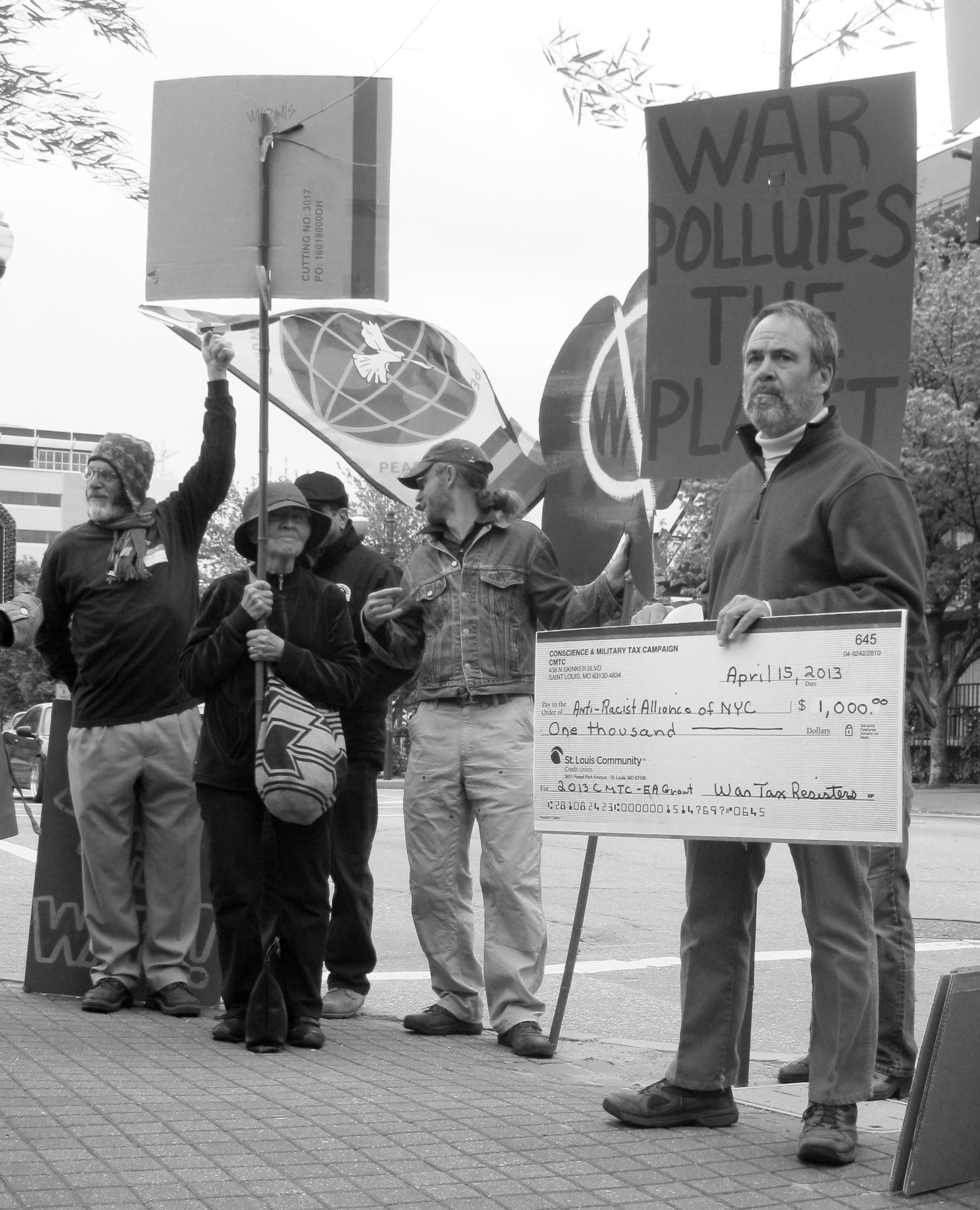 A man holds an oversized check for $1,000 made out to “Anti-Racist Alliance of N.Y.C.” from Conscience & Military Tax Campaign