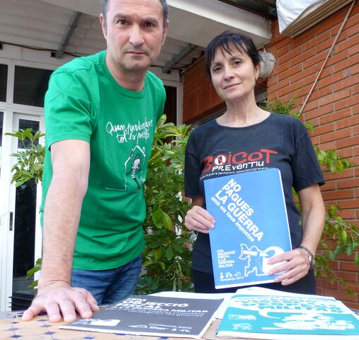 Tirs Llorens and Jùlia Moltó stand facing the camera. Jùlia Moltó holds a book titled “No Pagues La Guerra” (Don’t Pay for War)