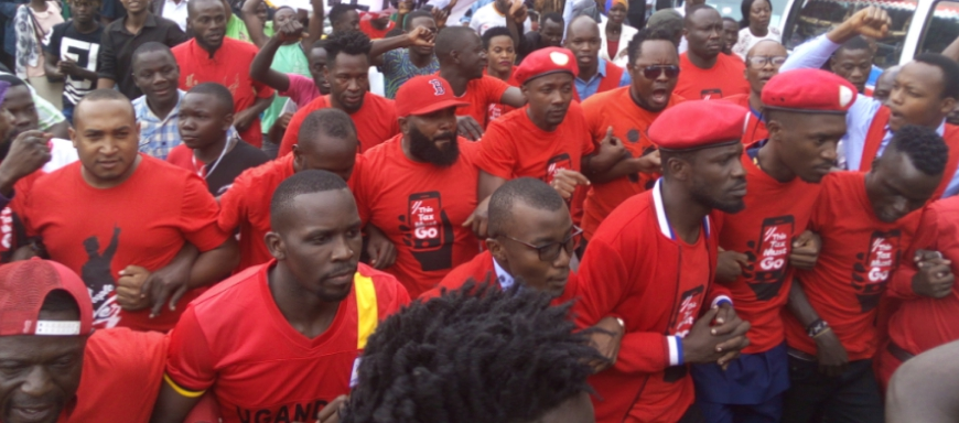 protest marchers in Uganda, with their elbows hooked together, dressed in red shirts featuring a smart phone screen that reads “This Tax Must Go”