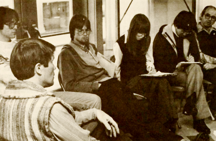 photo of six people seated inside on folding chairs near a doorway