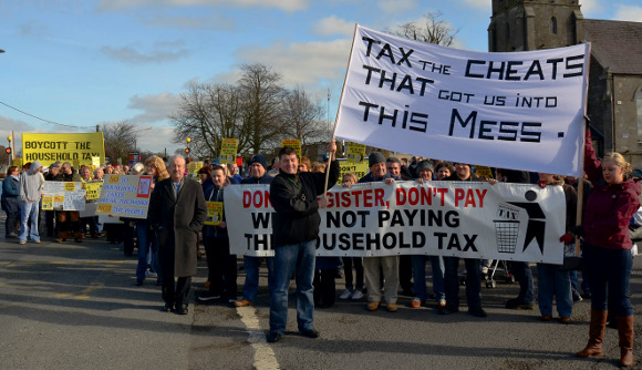protesters holding signs reading “Boycott the Household Tax,” “Don’t Register, Don’t Pay: We’re Not Paying the Household Tax,” and “Tax the Cheats that got us into this Mess.”