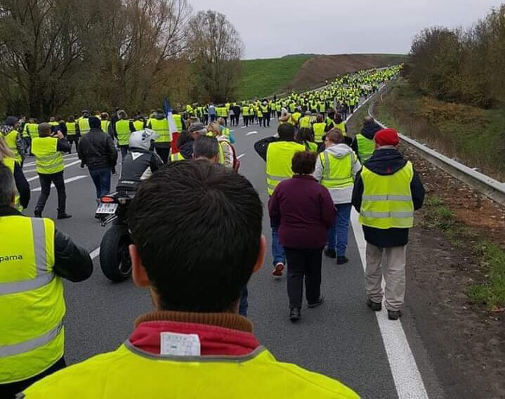 Hundreds of people wearing yellow vests march down a carless highway
